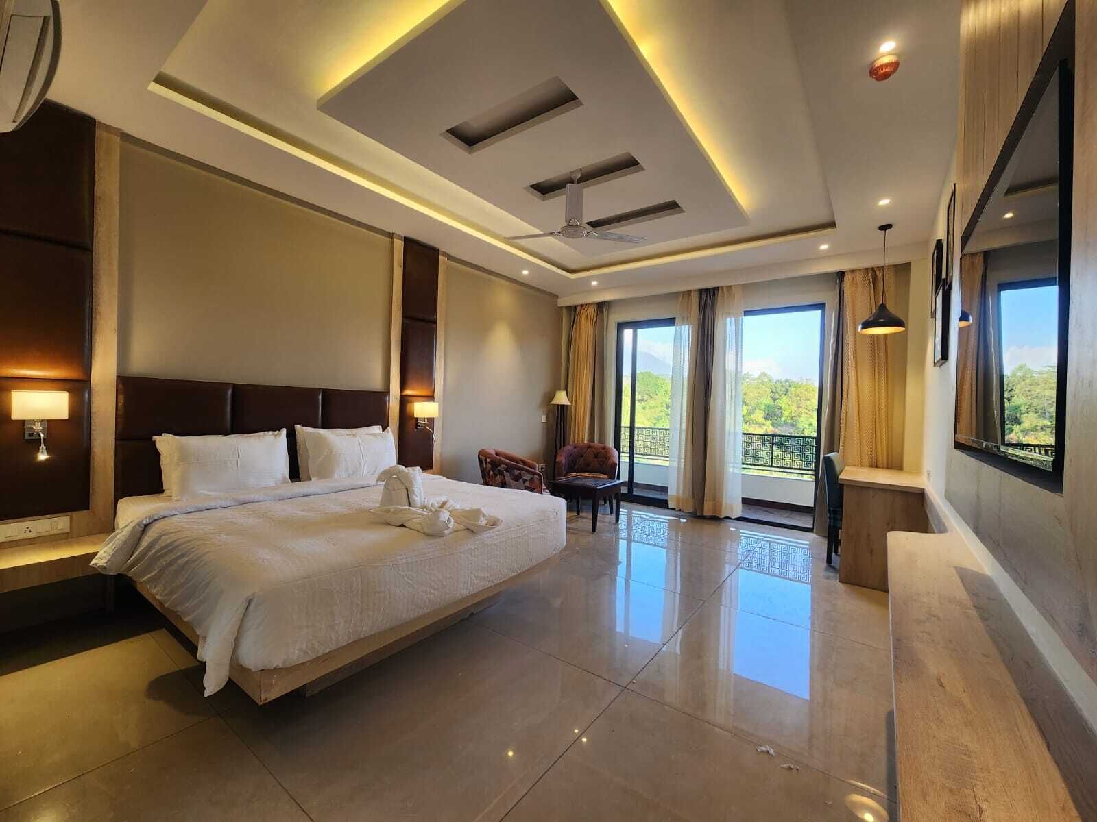 A modern hotel room with a large bed, a balcony with a view, and a ceiling fan.