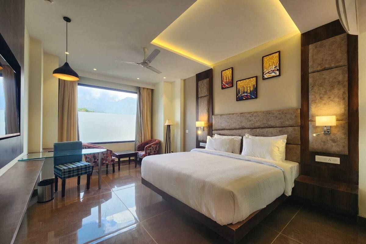 A hotel room with a large bed, a desk with a chair, a ceiling fan, and artwork on the walls.