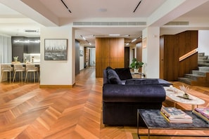 Another perspective of our inviting living space, capturing the seamless blend of the living room, sofa, kitchen, and a glimpse of a corridor. Experience the harmonious design of our Penthouse, where every corner reflects comfort, style, and a welcoming ambiance