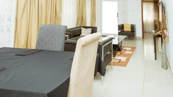 A modern hotel room with a dining area, a sofa, a chair, and a bed.