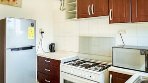Een kleine keuken met een koelkast, fornuis, oven, magnetron en een spoelbak.