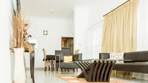 Een moderne woonkamer met een bank, salontafel en stoelen. Op de vloer staat een decoratieve vaas met gedroogde planten.