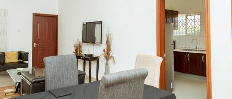 A dining area with a table set for four, a sofa, a TV, and a kitchen visible through an open door.