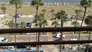 A beach view with palm trees, umbrellas, and a clear sky. - Finikoudes Beech front views Carisa Ithaki  (Larnaca)