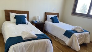 A hotel room with two beds, each with white linens and blue accents, a bedside table with a lamp, and a window providing natural light. - Finikoudes Beech front views Carisa Ithaki  (Larnaca)