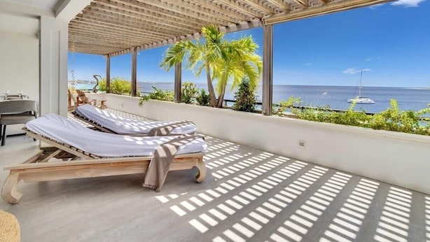 Una habitación luminosa con una cama de madera, ventanas amplias y vistas al mar.