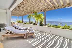A sunlit room with a wooden bed, large windows, and a view of the sea. - Playa Lechi Penthouse right by the Caribbean Sea (Kralendijk)
