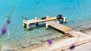 Un muelle de madera que se adentra en aguas azules y transparentes, con una pequeña construcción al final.