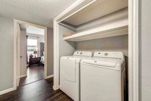 A laundry room with two white front-loading washing machines and a shelf above them. - I36 - Apt|Yard|11mi to Fair Park|Sleeps 4 (Irving)