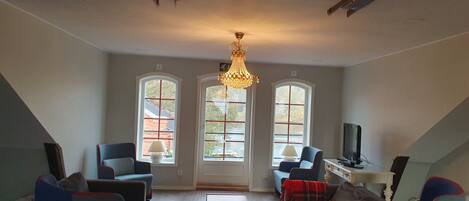 Amplia sala de estar con candelabro, ventanas grandes y televisor.