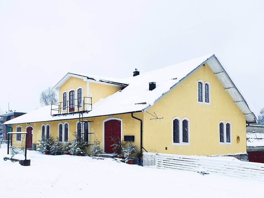 Un edificio amarillo con puerta y ventanas rojas, rodeado de nieve.
