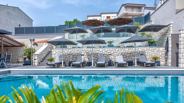 A swimming pool with lounge chairs and umbrellas, surrounded by stone walls and a staircase.