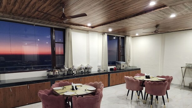 A dining area with a long counter, multiple chairs, and a view of the sunset through large windows. - Him Hilton Luxury Hotel (Krishangarh)