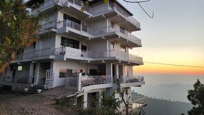 A multi-story hotel with balconies, a car parked in front, and a view of the landscape. - Him Hilton Luxury Hotel (Krishangarh)