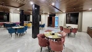 A modern dining area with marble flooring, wooden ceiling, and variously colored chairs and tables. - Him Hilton Luxury Hotel (Krishangarh)