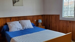 Une chambre à coucher avec une tête de lit en bois, un lit avec une literie bleue et blanche, deux lampes de chevet et une fenêtre donnant sur une clôture.