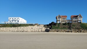 Un bâtiment situé sur la côte, avec une façade blanche et un toit rouge, qui se trouve sur une plage de sable, avec une falaise rocheuse en arrière-plan.