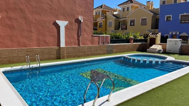 En swimmingpool med två stegar, omgiven av en röd mur och en grön gräsmatta.