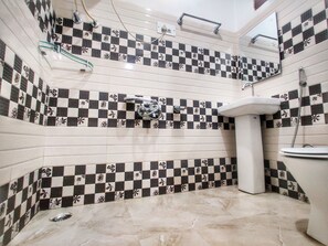 A bathroom with checkered tile walls, a pedestal sink, and a shower area. - Hotel Nissar (Srinagar)
