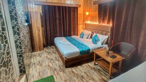 A bedroom with a wooden bed, a small table with a lamp, and a ceiling fan. - Hotel Nissar (Srinagar)