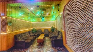 A room with wooden walls, a ceiling fan, a seating area with sofas and a table, and a patterned floor. - Hotel Nissar (Srinagar)