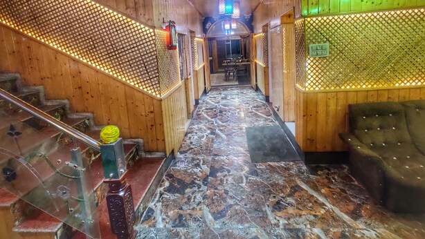 A hallway with wooden walls, a marble floor, and a staircase with a glass railing. - Hotel Nissar (Srinagar)