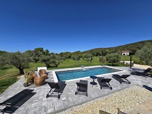 A rectangular swimming pool with a tiled deck, surrounded by lounge chairs and a small table. - Olive Garden Paradise with Swimming pool (Rovinj)