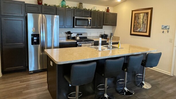 Una cocina moderna con una isla central, taburetes de bar, electrodomésticos de acero inoxidable y un microondas.