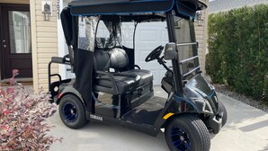 Un carro de golf negro estacionado frente a una casa con garaje.