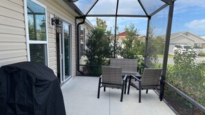 Un patio cubierto con una parrilla, muebles de mimbre y vistas a casas vecinas.
