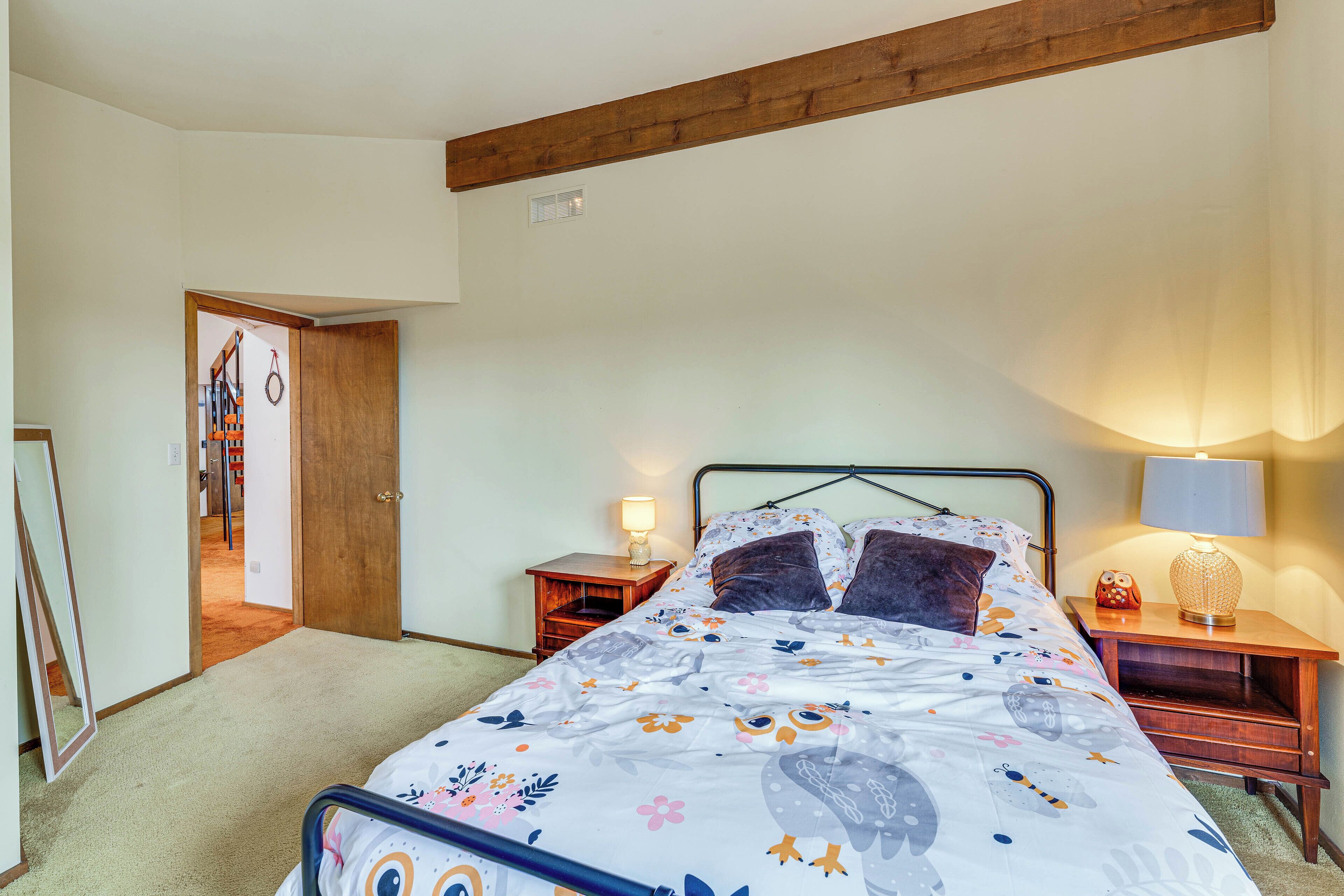 A bedroom with a bed, wooden headboard, nightstands, and a door leading to another room.