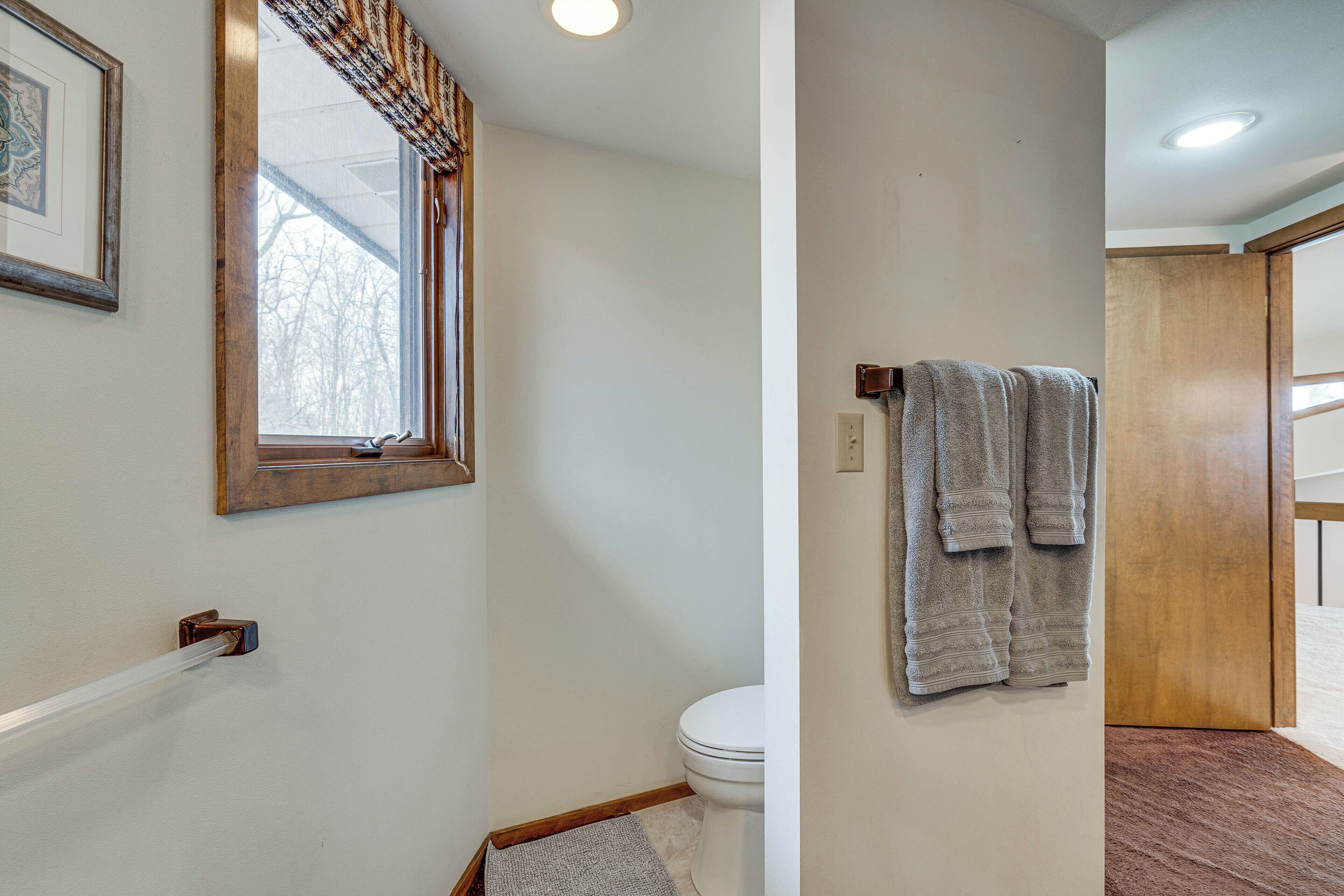A bathroom with a toilet, a towel rack, a window with a curtain, and a wooden door.