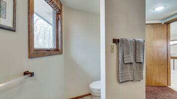 A bathroom with a toilet, a towel rack, a window with a curtain, and a wooden door.