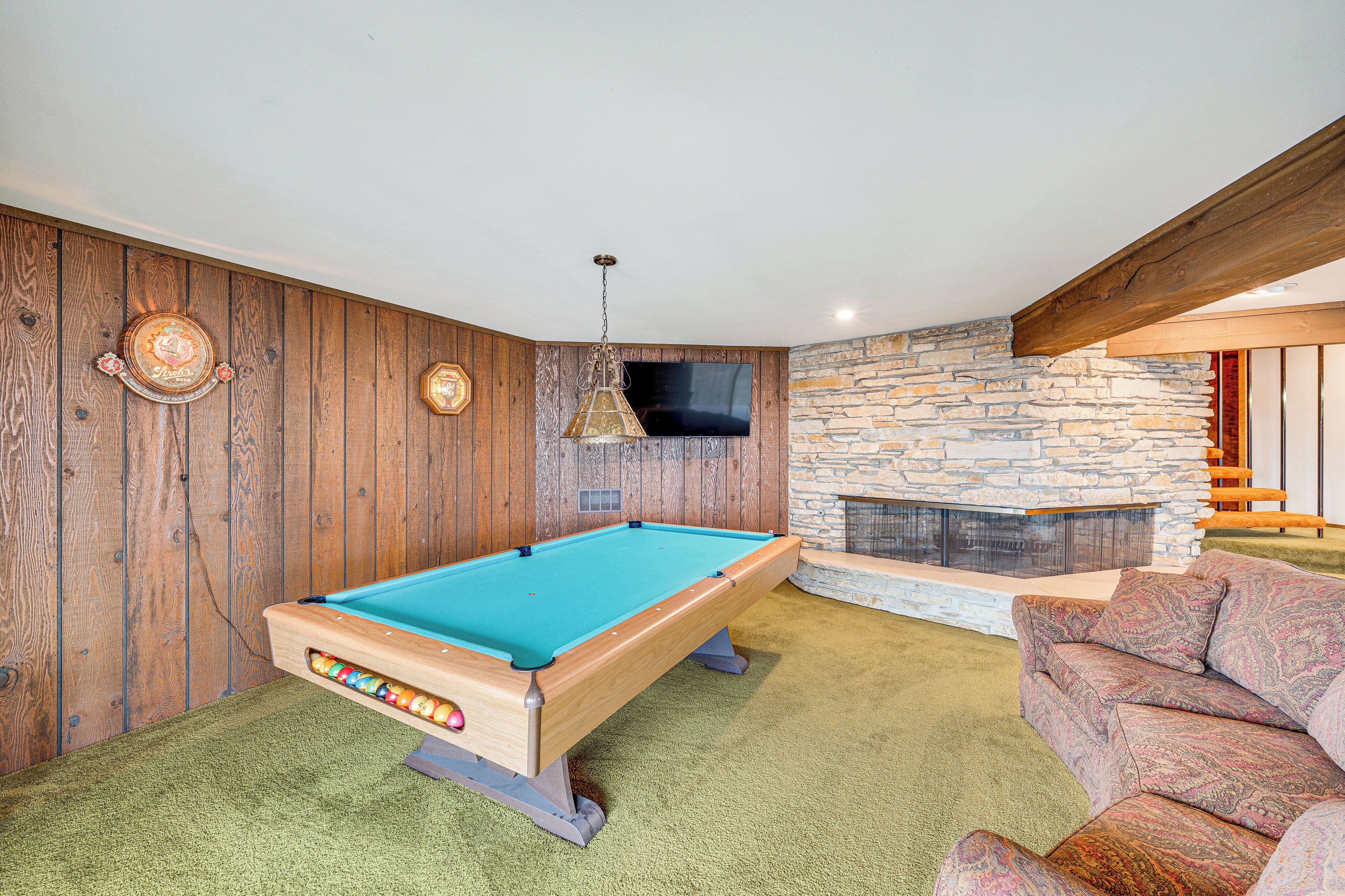Een pooltafel in een kamer met houten wanden, een stenen openhaard en een bank.