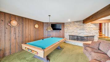 Een pooltafel in een kamer met houten wanden, een stenen openhaard en een bank.