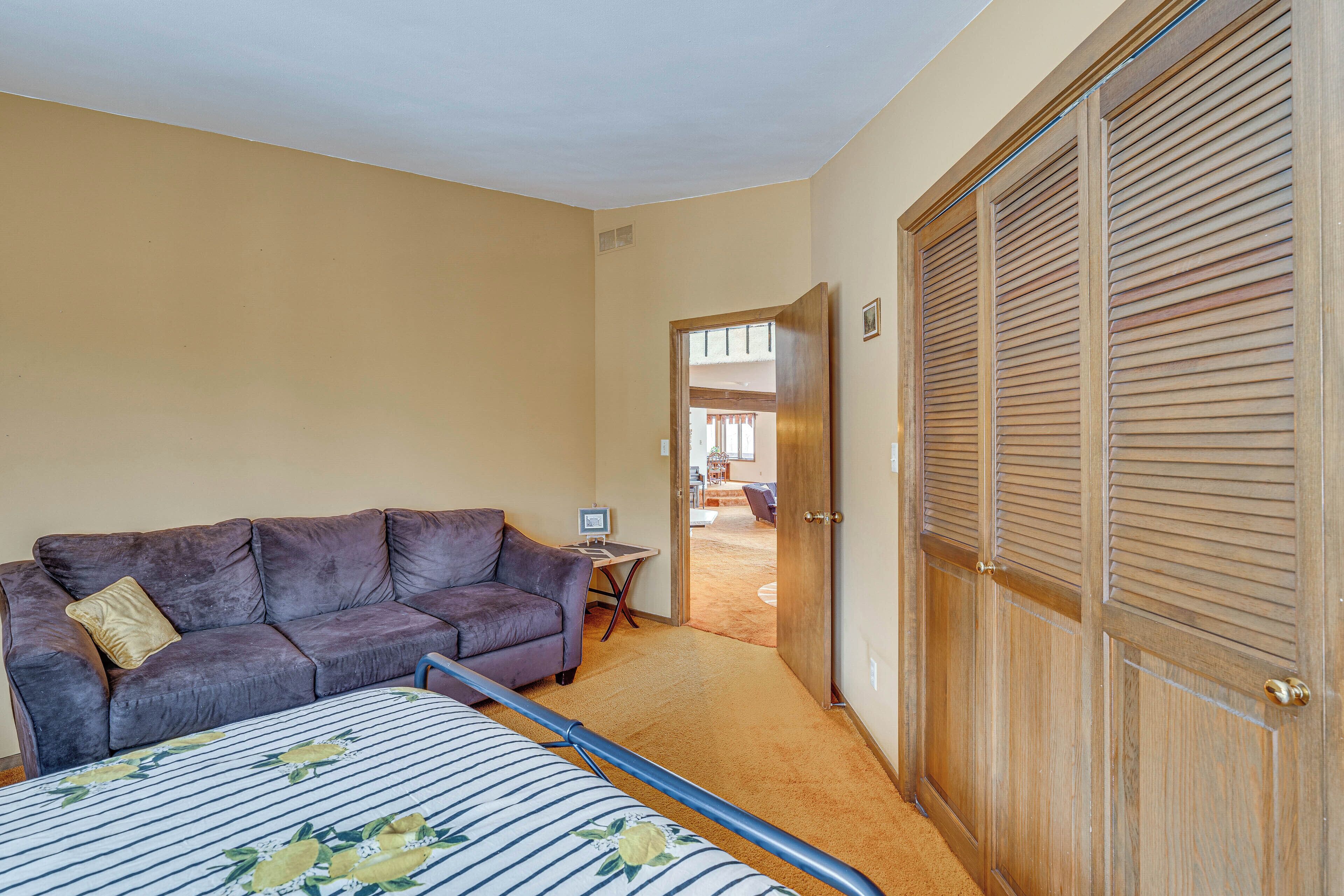 Une pièce comprenant un lit, un canapé, une armoire en bois et une porte donnant sur une autre pièce.