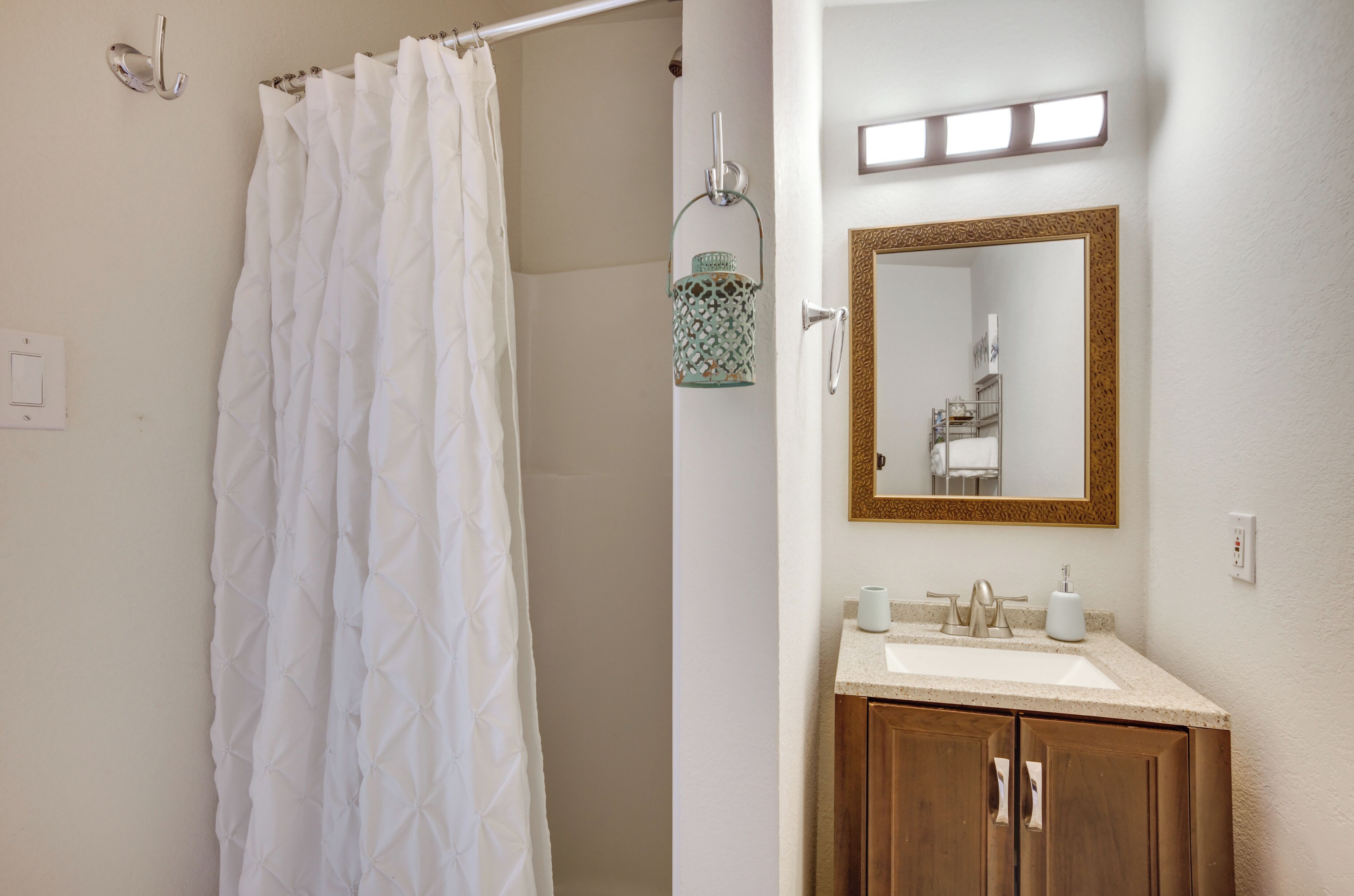 A bathroom with a shower curtain, a sink, a mirror, and a hanging lantern.
