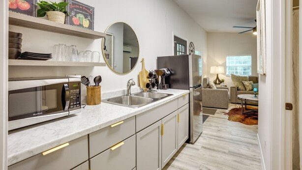 Una cucina moderna con forno a microonde, lavello e frigorifero in acciaio inossidabile. Sono presenti mensole con oggetti decorativi e un grande specchio sopra il bancone.