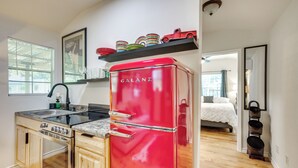 A compact kitchen with a red Galanz refrigerator, wooden cabinets, a stainless steel sink, and a window with blinds. - Cozy Montgomery Cottage w/ Porch, Near Lake Conroe (Montgomery)
