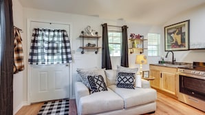 A cozy living room with a sofa, a coffee table, and a kitchen area with a stove and shelves. - Cozy Montgomery Cottage w/ Porch, Near Lake Conroe (Montgomery)
