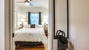 A bedroom with a bed, two bedside lamps, a ceiling fan, a window with curtains, and a wall-mounted basket. - Cozy Montgomery Cottage w/ Porch, Near Lake Conroe (Montgomery)