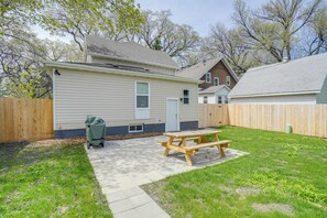 A backyard with a picnic table, a wooden fence, and a house with a garage. - Dog-friendly Home < 1 Mi to Downtown Fargo! (Fargo)