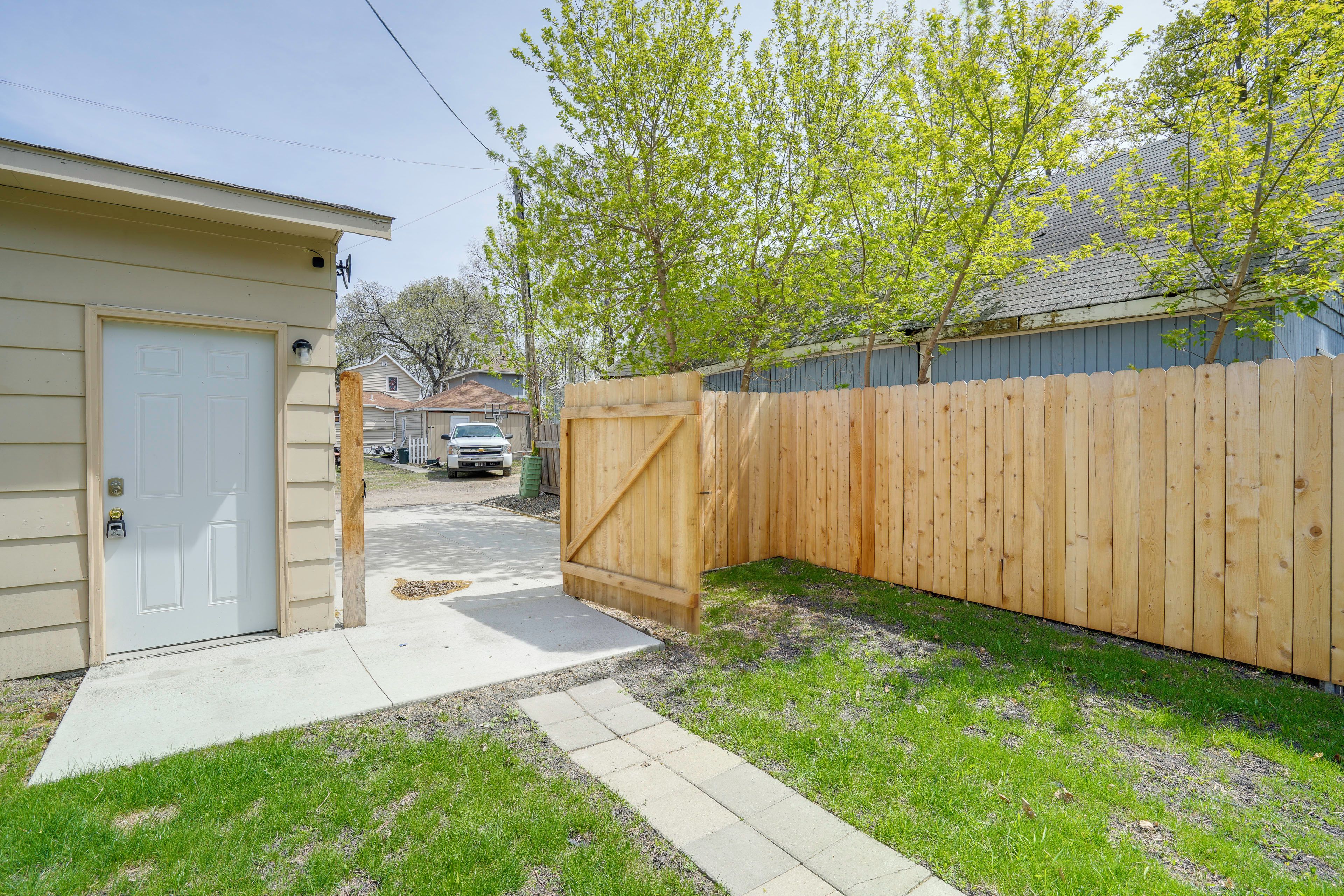 Un jardin à l’arrière d’une maison, avec une clôture en bois, un garage et une allée menant à un véhicule stationné.