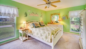 Une chambre à coucher comprenant un lit, des tables de chevet, un ventilateur de plafond, une fenêtre avec des rideaux et une vue sur l’extérieur.