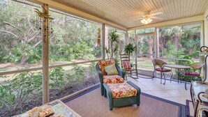 Une véranda donnant sur un jardin, une chaise en osier avec un coussin et une table avec des chaises.