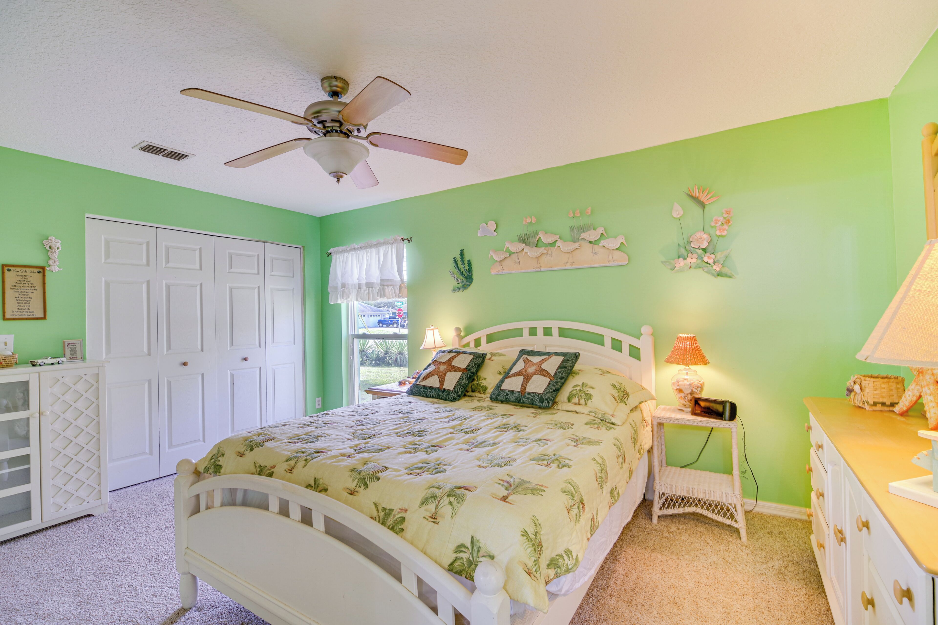 A bedroom with a bed, a ceiling fan, a dresser, a nightstand, and a window with curtains.