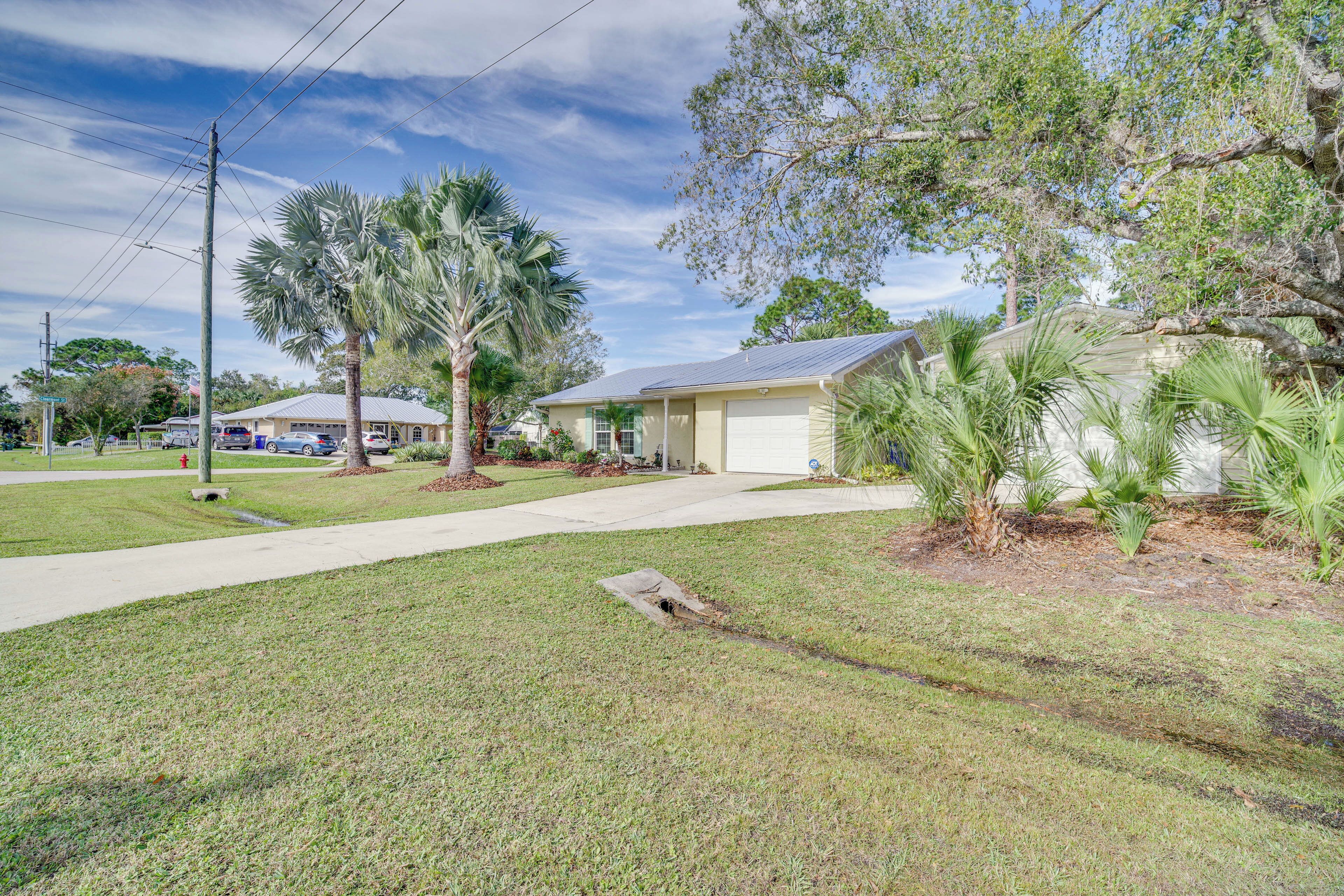 A residential property with a well-maintained lawn, palm trees, and a single-story house with a garage.