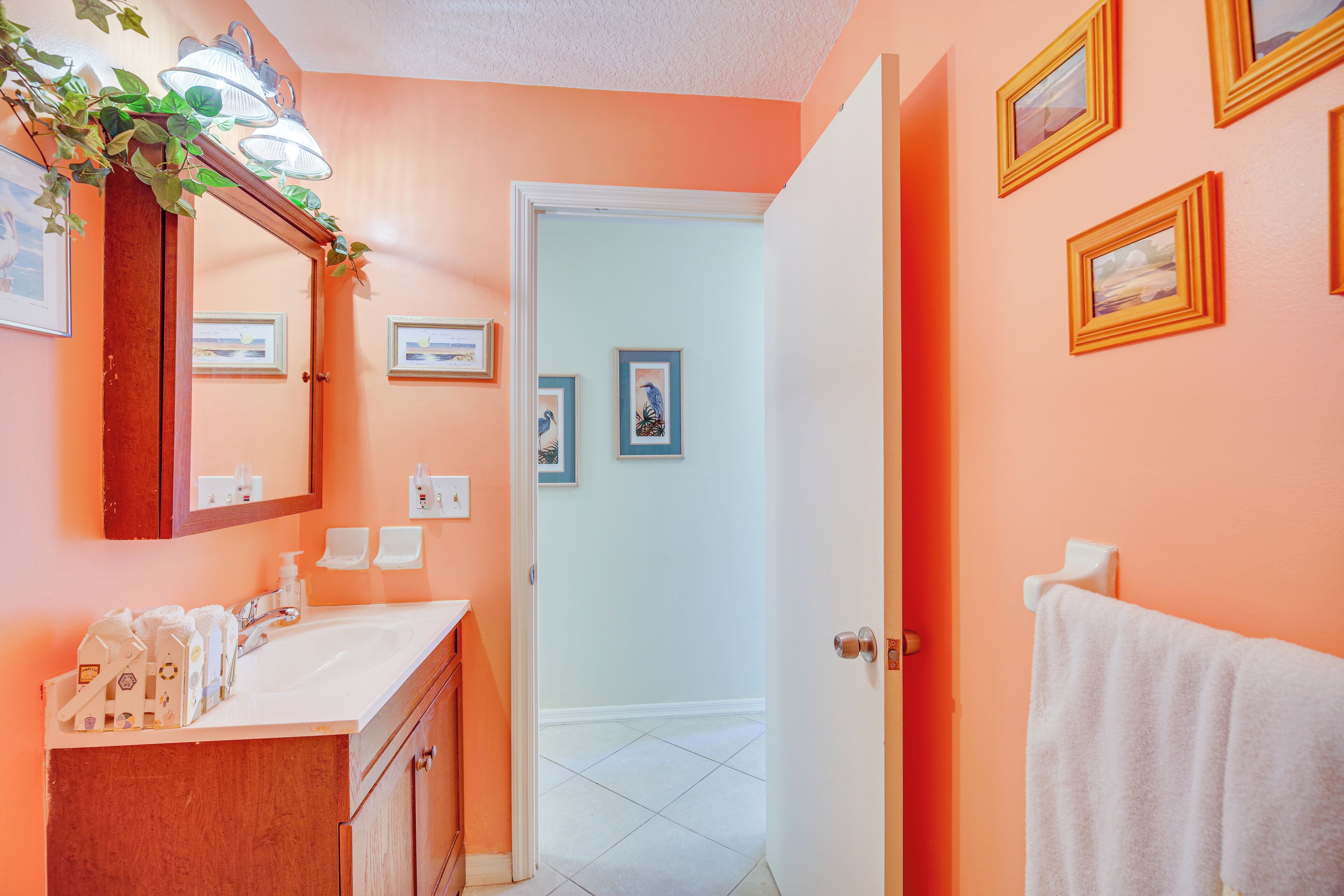 A bathroom with a wooden vanity, a mirror, and a sink. There are framed pictures on the wall and a towel hanging on the door.