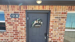 A brick building with a dark grey door, a welcome wreath, and a number sign '15130' on the wall.