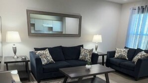A modern living room with two dark sofas, a coffee table, and a large mirror on the wall.